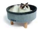 تتمدد قطة تابي ذات فراء ناعم داخل سرير قطط دائري علوي، يتميز ببطانة ناعمة من الفراء وساق خشبية أنيقة. يتناغم التصميم العصري مع ديكور منزل القطة الأنيق.
